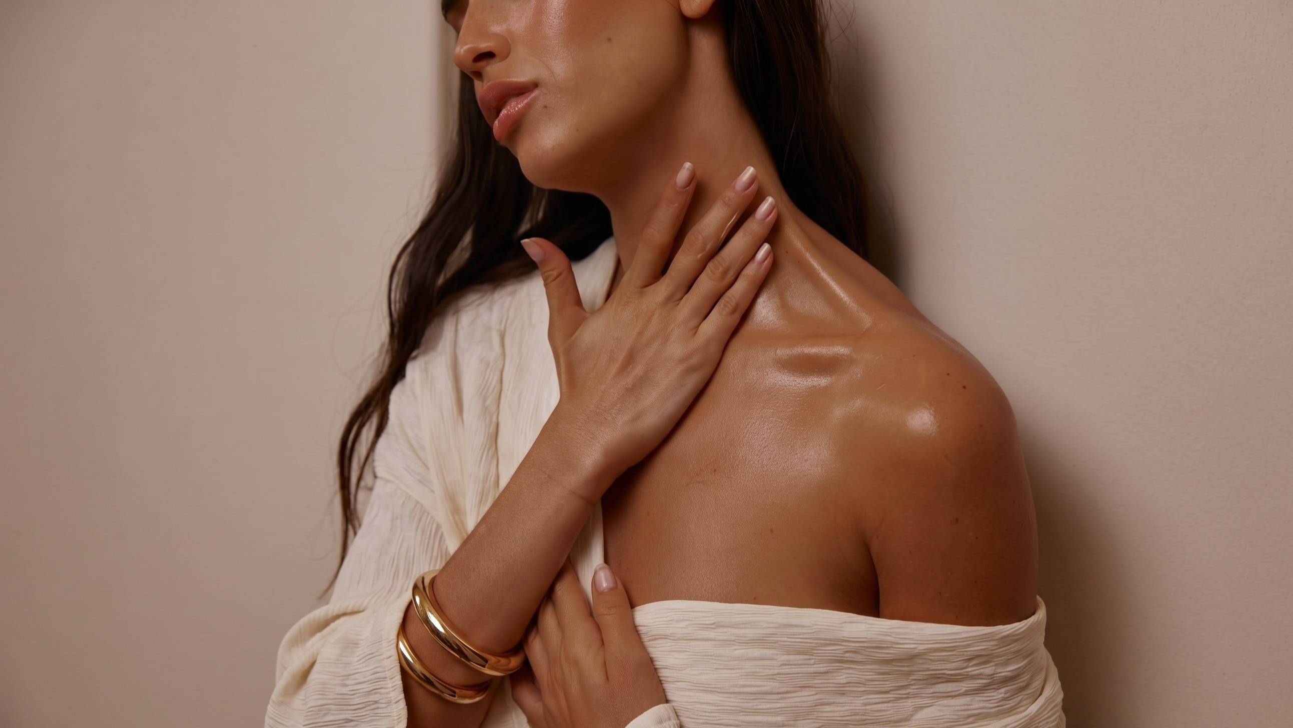 Woman with smooth skin and gold bracelets against a beige background